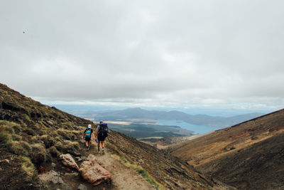 Rear view of man with son hiking on mountain against cloudy sky