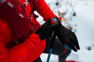 Top cropped view of sportswoman with trekking poles checking fitness watch on cold winter day.
