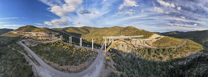 Drone panoramic view of a new bridge construction site over the old road and dramatic sky background