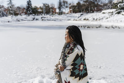 Thoughtful woman with shawl looking away while standing in snow covered land