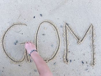 Cropped hand of person making alphabets on sand at beach