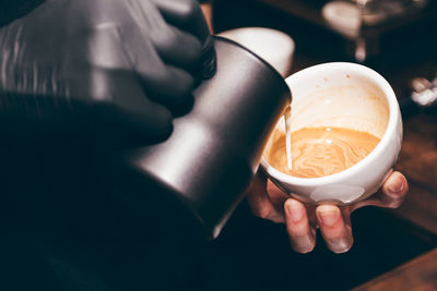 Cropped image of barista adding milk in coffee at shop