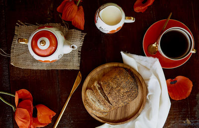 Poppy seed bun with cup of tea and milk among poppies flowers and dishes with poppies ornaments. 