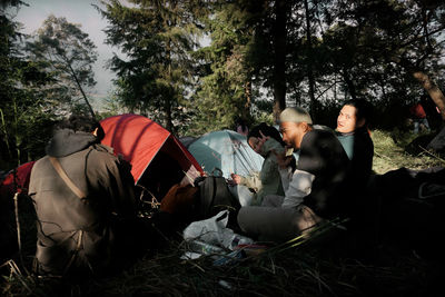People sitting on land by tents in forest