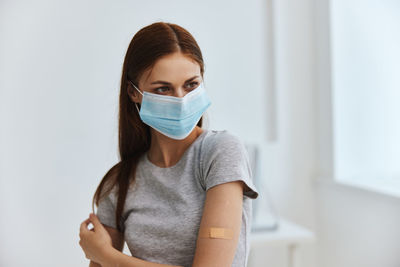 Young woman wearing protective mask while standing against white background