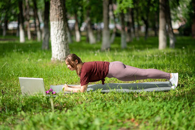 Young girl having online workout outdoors using laptop. pilates or yoga video lesson on internet. 