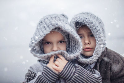 Girl in knitted grey hat hugging her frozen smaller brother