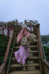 Rear view of man standing on staircase against clear sky