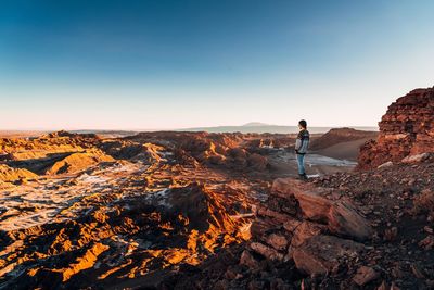 Side view of mid adult woman standing on rock against clear sky during sunset