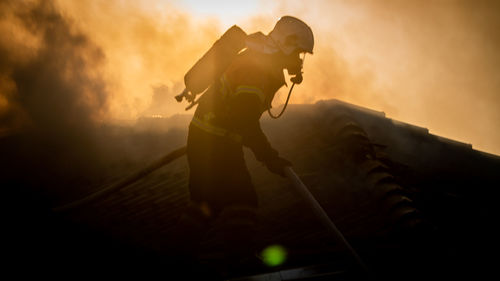 Side view of firefighter holding hose during sunset