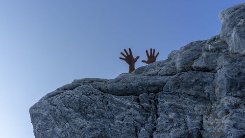 Cropped hands of person on rock against clear blue sky