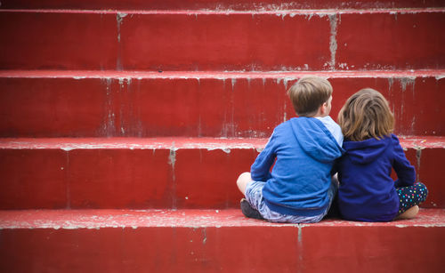 Rear view of people sitting against red wall