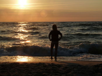 Rear view of silhouette man standing on beach during sunset