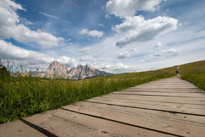 Wooden hiking trail at seiser alm with sassolungo mountain group in front of blue sky with clouds