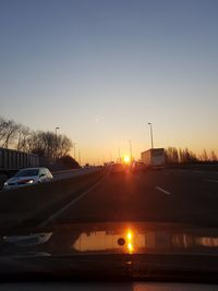 Cars on road against clear sky during sunset