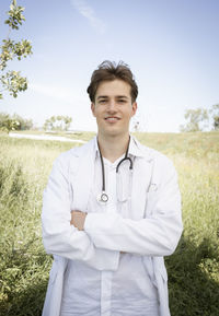 Portrait of smiling female doctor standing against sky