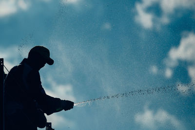 Silhouette of man splashing water against cloudy sky