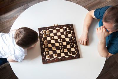 View from above dad and son are playing a board game of chess. time and games with children.