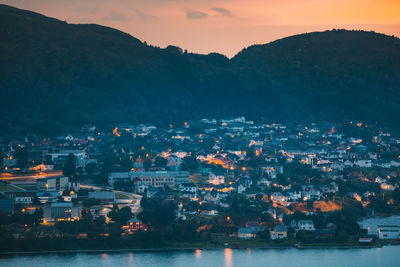 Illuminated cityscape by sea against sky during sunset