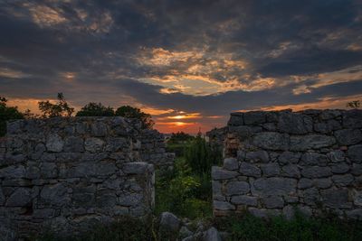 Stone wall by old building against sky during sunset