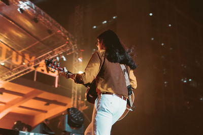 Woman standing by illuminated lighting equipment at night