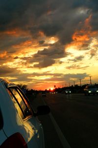 Cars on road against dramatic sky during sunset