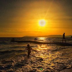 Silhouette people on beach against sky during sunset