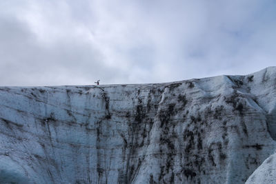 Anonymous tourist in outerwear doing headstand on top of vatnajokull glacier against cloudy gray sky on cold winter day in iceland