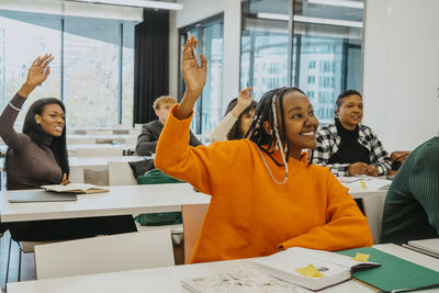 Female students raising hands while sitting in classroom