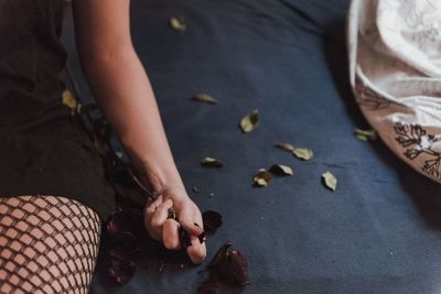 Midsection of woman holding wilted rose while sitting on bed