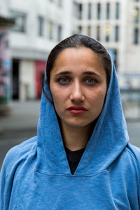 Portrait of woman wearing hoodie standing against building in city