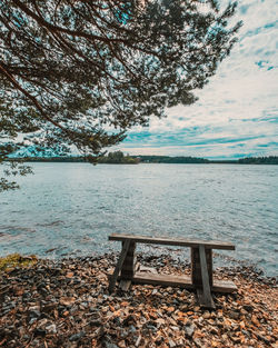 Bench by lake against sky during autumn