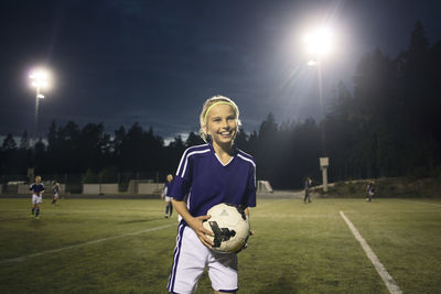 Happy of girl standing with soccer ball on field against sky at night