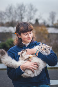 Beautiful brunette is holding in her arms grey and white princess of ragdoll breed cat