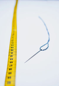 High angle view of tailoring tools like needle, tape measure and yarn against white background.