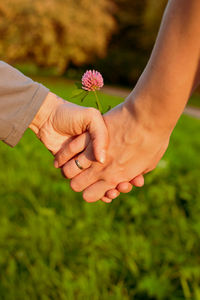 Cropped image of couple holding hands with flower