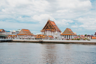 View of buildings by river against cloudy sky