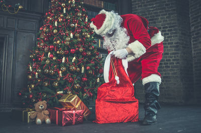 Man wearing santa claus costume holding christmas present at home