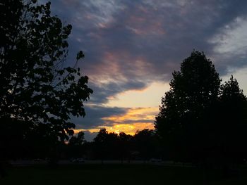 Silhouette trees on field against dramatic sky