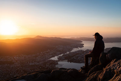 Man sitting on rock against sky at sunset