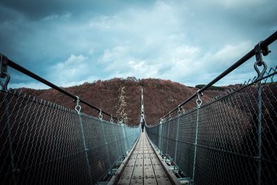 Footbridge over chainlink fence against sky