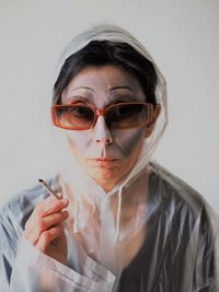 Portrait of woman wearing sunglasses holding cigarette against white background