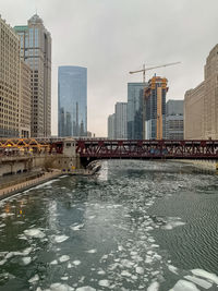 Bridge over river by buildings against sky in city