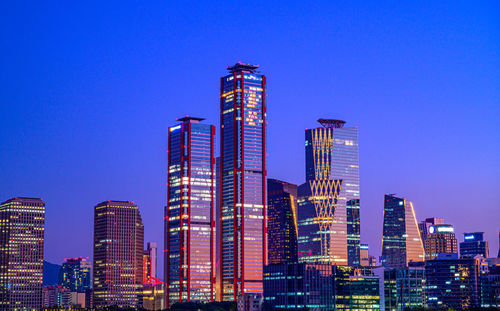 Illuminated modern buildings against clear blue sky