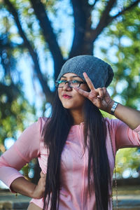 Portrait of young woman showing peace sign while standing at park