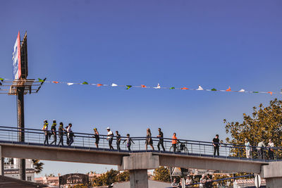 People on bridge against clear blue sky