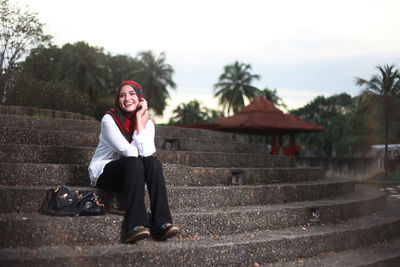 Cheerful young woman wearing hijab while sitting on steps