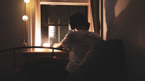 Rear view of man sitting on bed at home