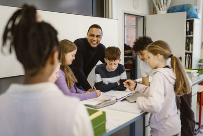 Happy teacher with multiracial students at desk in classroom