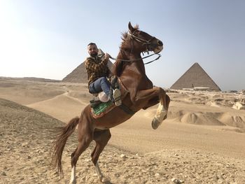 Man riding horse in desert against sky